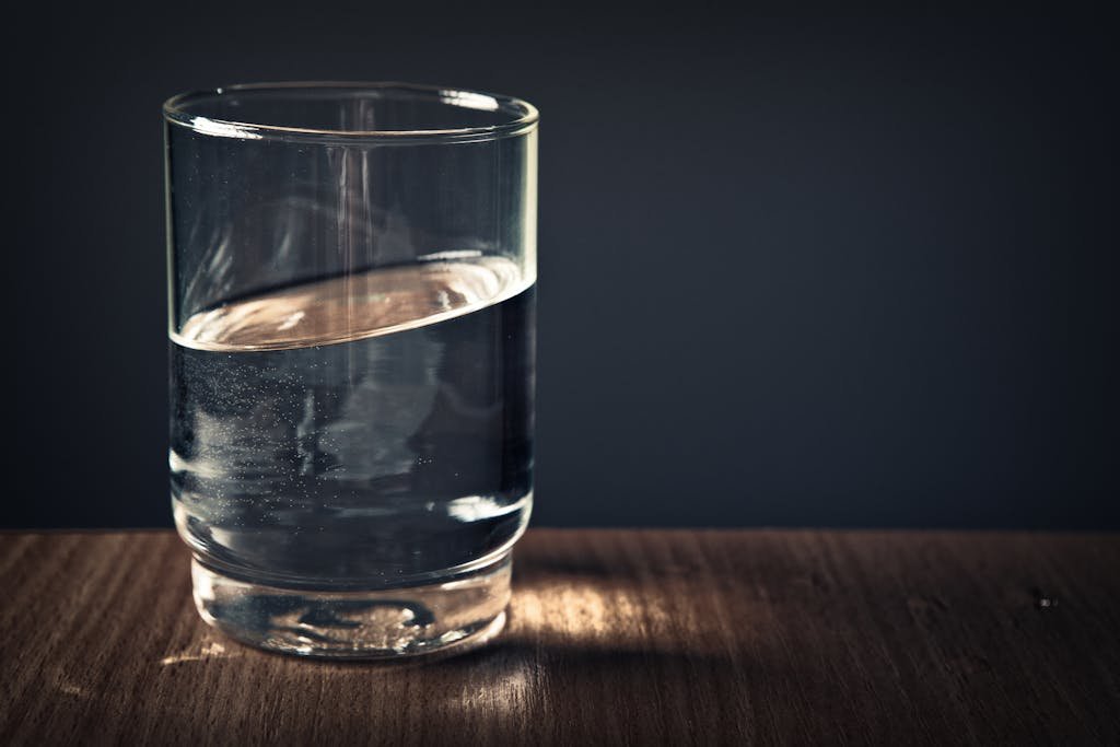 A clear glass of water sitting on a wooden table against a dark background.